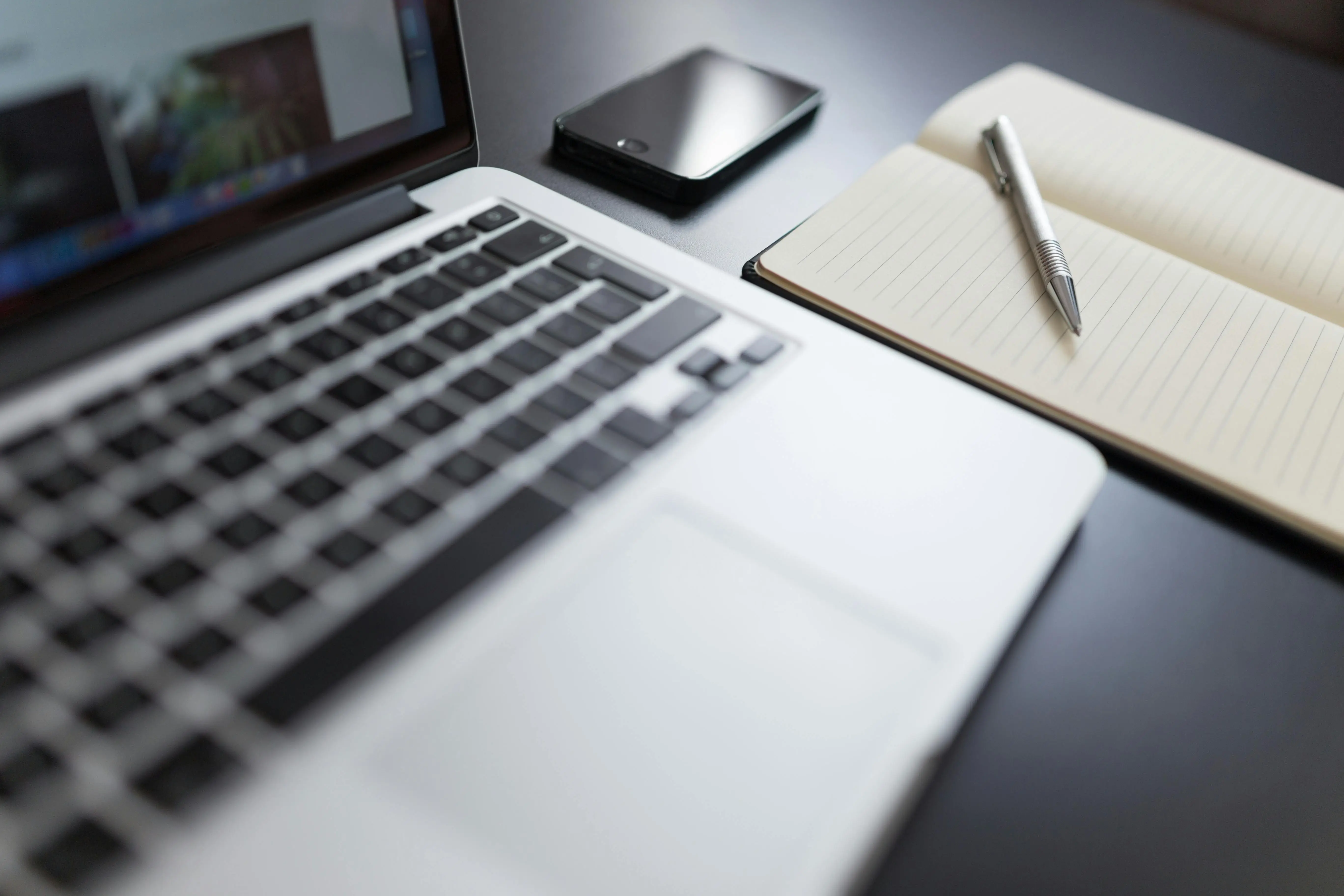 A laptop, phone and notebook on a desk